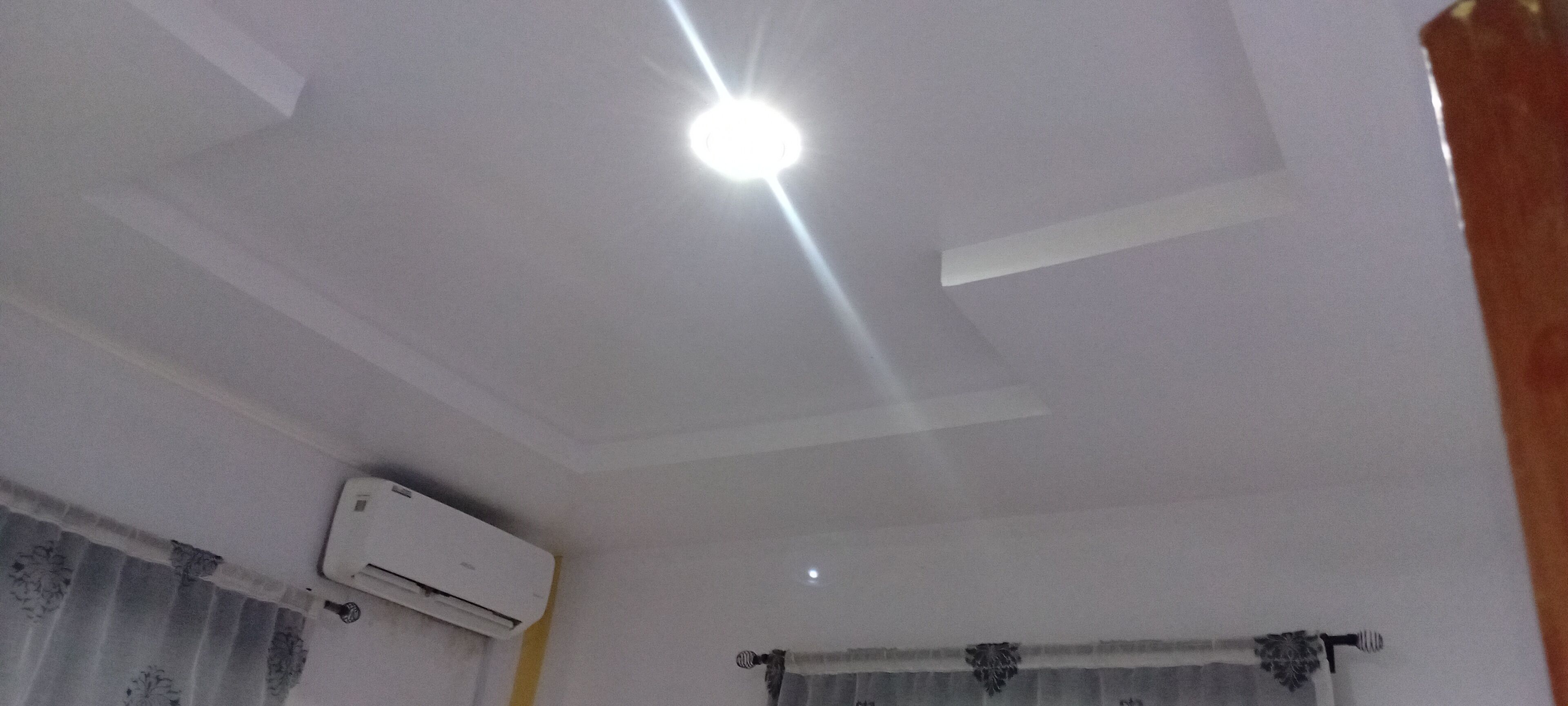A room with a white ceiling, an air conditioning unit mounted on the wall, and a window with a curtain.