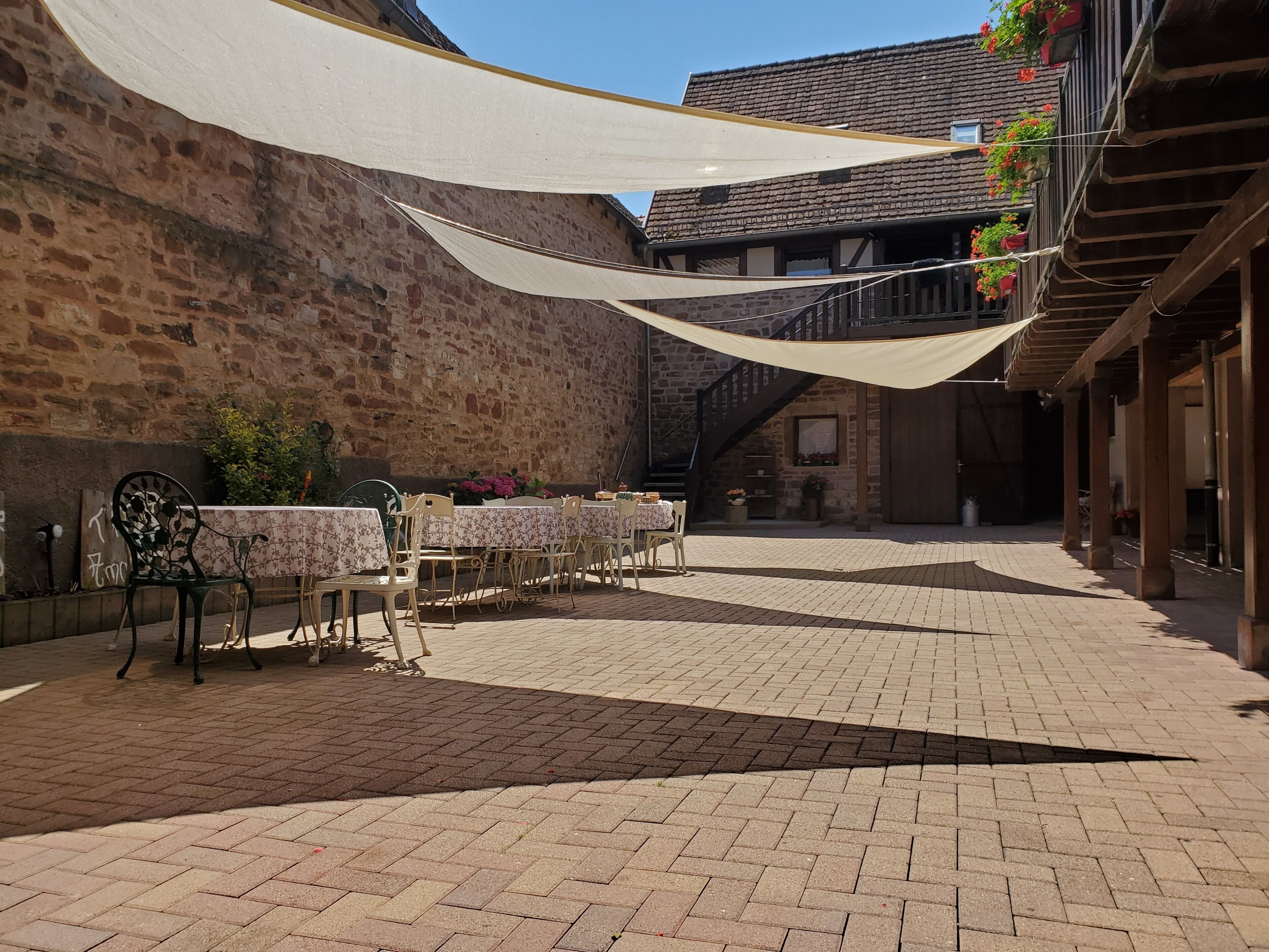An outdoor patio with tables and chairs, a stone wall, and a wooden building with balconies.