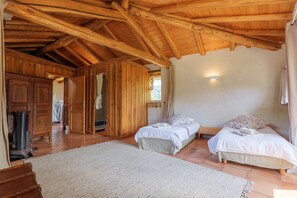 Interior de una cabaña de madera con dos camas, un tapete grande y techo de madera.
