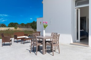 Un patio con mobili in vimini, un tavolo bianco e un vaso con fiori.