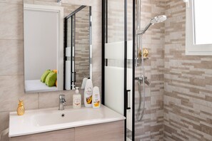 Un bagno con box doccia in vetro, lavandino con articoli da toilette e specchio.