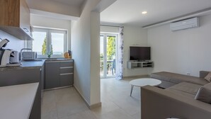 A modern kitchen with a built-in microwave, a dining area with a white table, a sofa, and a TV mounted on the wall. - Modern vacation apartment with fantastic views and swimming pool (Crikvenica)