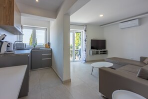 A modern kitchen with a built-in microwave, a dining area with a white table, a sofa, and a TV mounted on the wall. - Modern vacation apartment with fantastic views and swimming pool (Crikvenica)