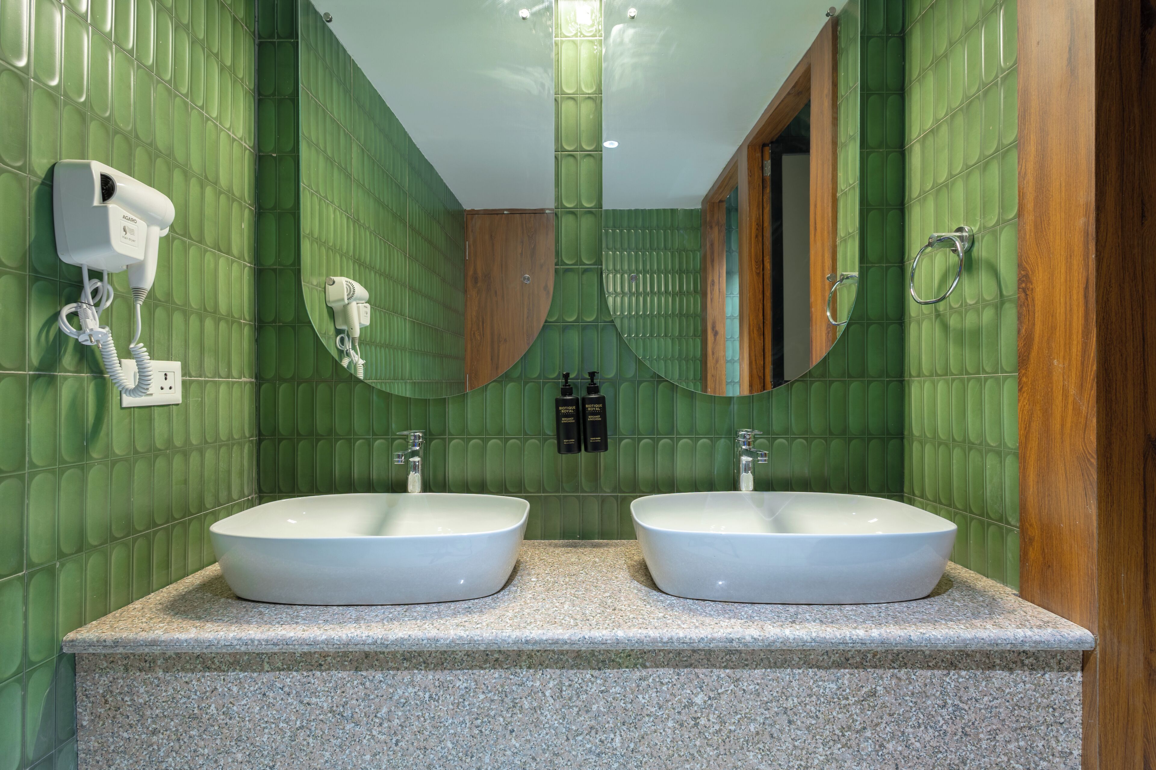 Un baño con paredes de azulejos verdes, dos lavamanos, un espejo y un secador de pelo.