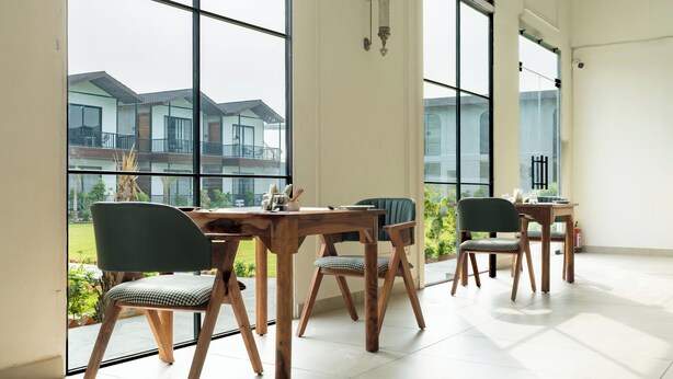 A room with large windows, wooden furniture, and a view of residential buildings. - Aayovea Resort Ayodhya Near Ram Mandir & Saryu River (Ayodhya)
