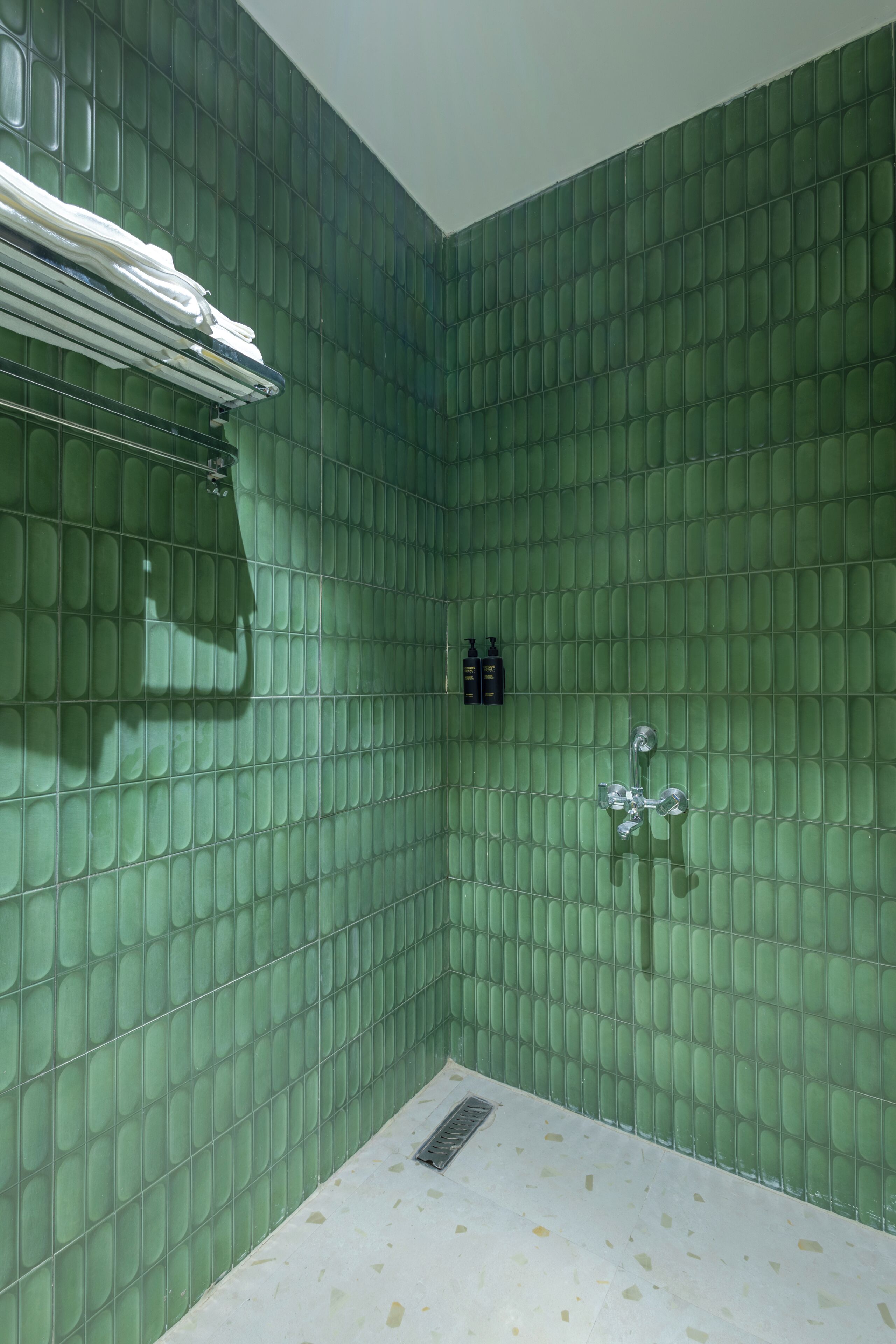 Un baño con paredes de azulejos verdes, una ducha y un perchero.