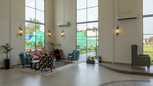 A spacious lobby with large windows, a seating area with chairs and a sofa, and a fire extinguisher near the windows. - Aayovea Resort Ayodhya Near Ram Mandir & Saryu River (Ayodhya)