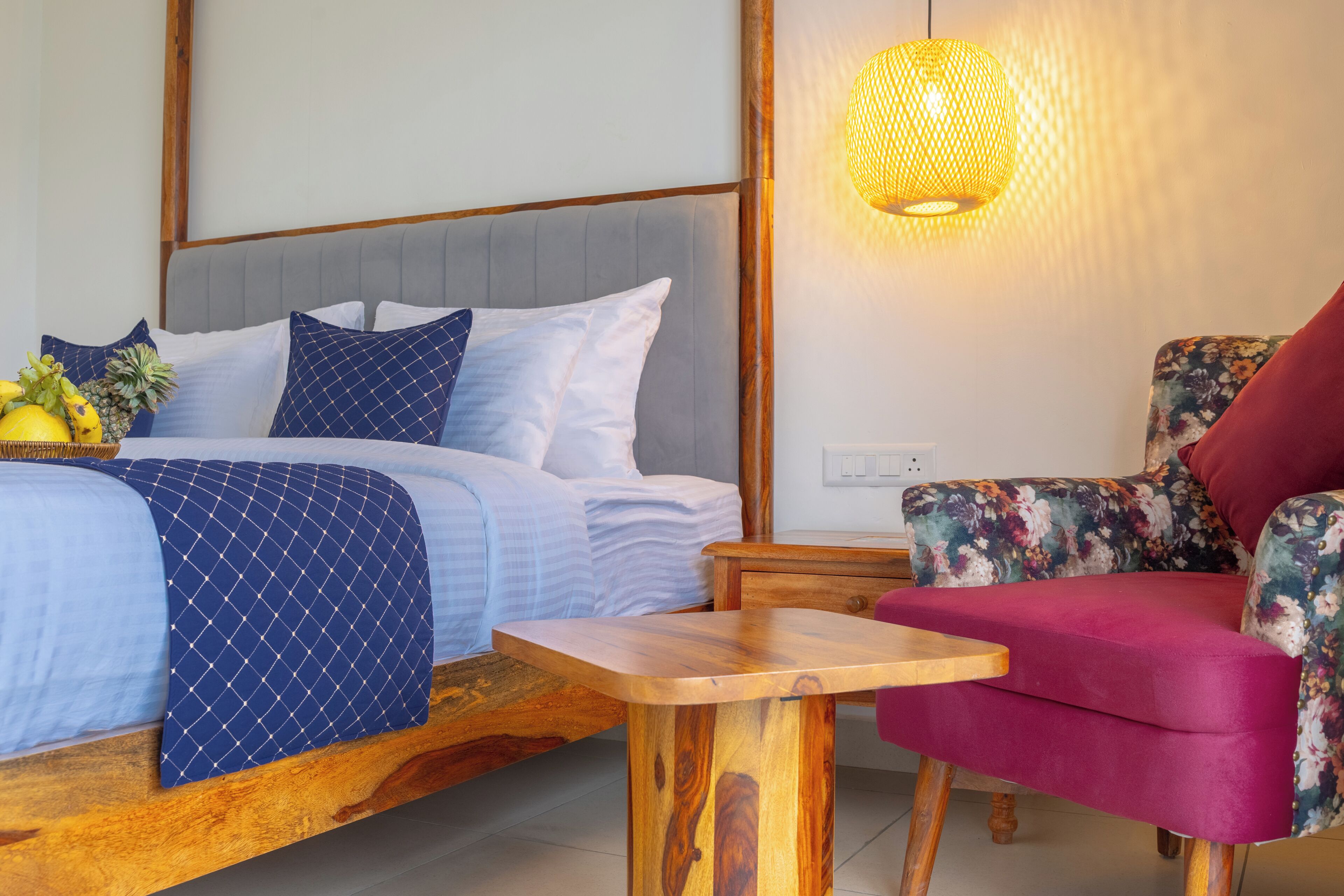 A bedroom with a bed, a wooden nightstand, a chair, and a hanging light fixture.
