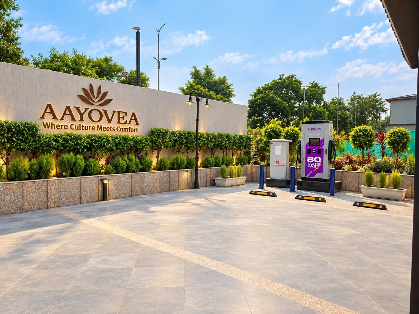 A modern entrance with a sign reading 'AAYOVEA Where Culture Meets Comfort,' a solar-powered electric vehicle charging station, and a well-maintained landscaped area.