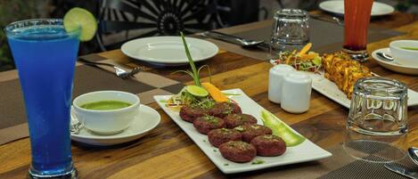 A dining table with a plate of food, a glass of blue drink, a bowl of green soup, and a tall glass of red drink.