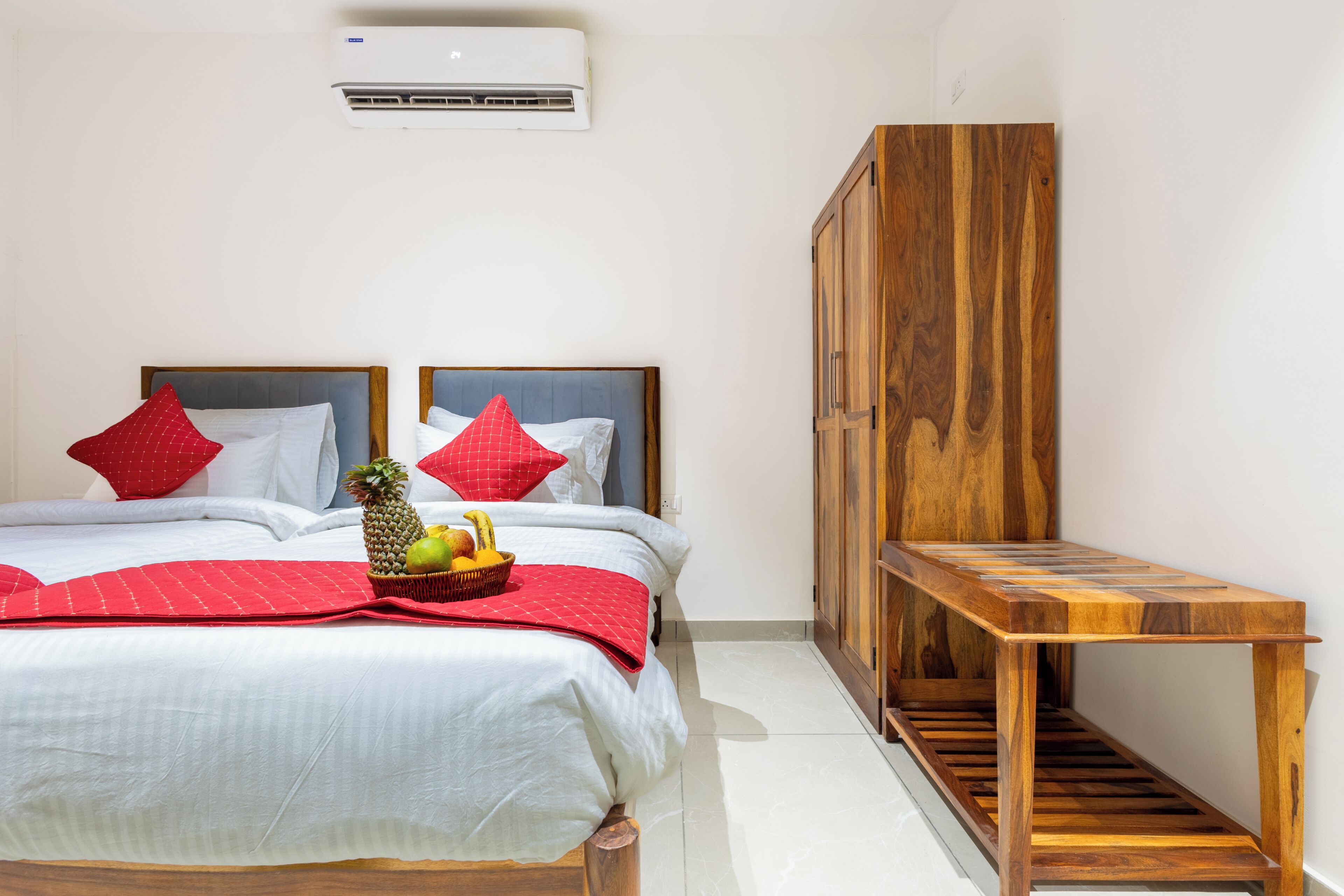 A hotel room with a bed, a wooden bench, and an air conditioning unit.