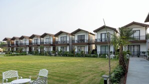 A row of modern multi-story buildings with balconies, a well-maintained lawn, and outdoor seating. - Aayovea Resort Ayodhya Near Ram Mandir & Saryu River (Ayodhya)