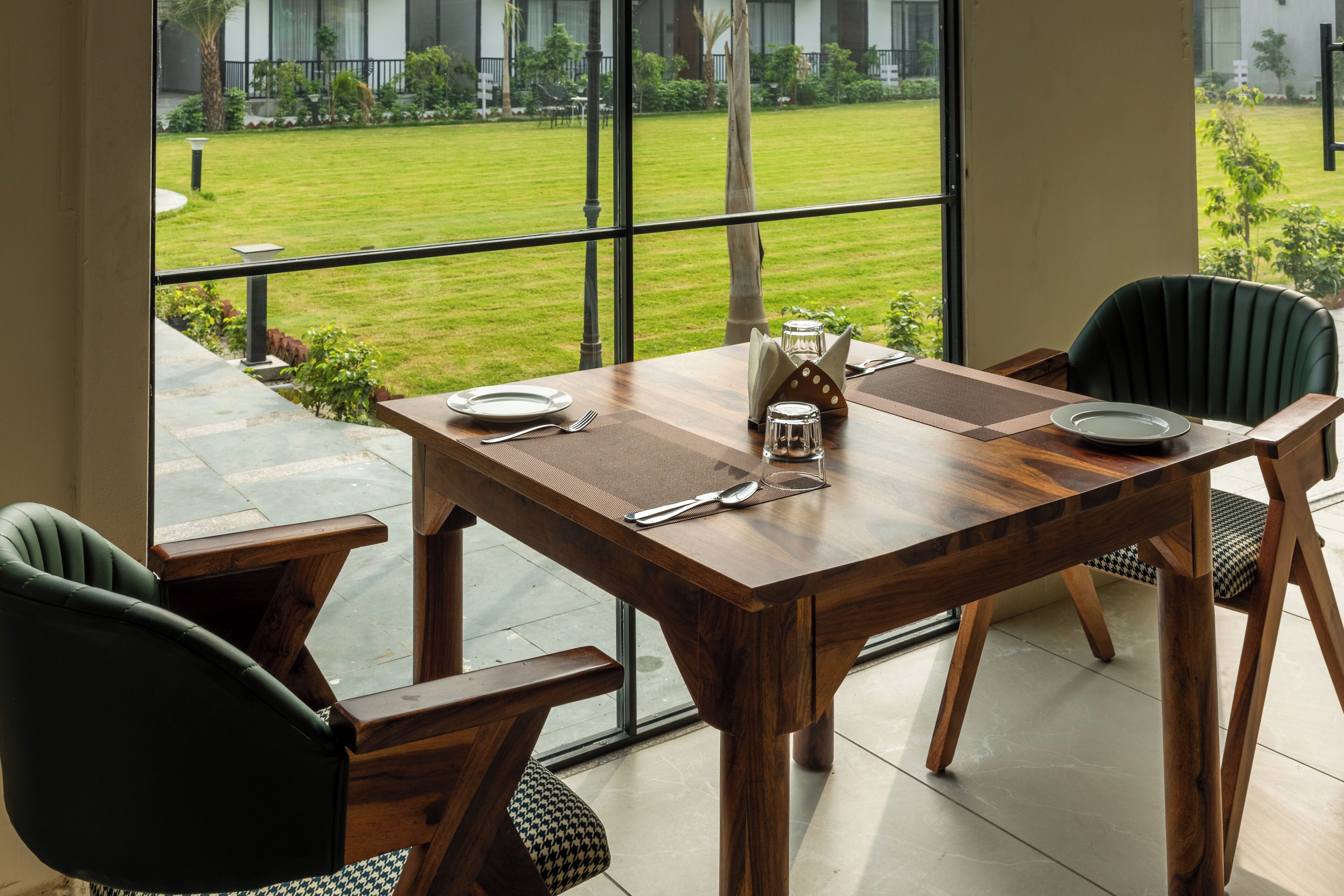 Un coin repas avec une table en bois, des chaises et une vue sur une pelouse bien entretenue, visible à travers de grandes fenêtres.