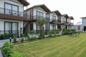 Un hotel moderno de varios pisos con balcones, mobiliario exterior y un césped bien cuidado.