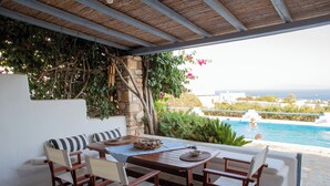 Un área de estar al aire libre con vista a la piscina, suelo de piedra y una pérgola de madera.