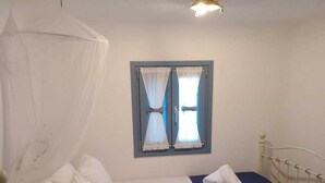 Una cama individual con dosel, un ventanal con cortinas y una mesita de noche con lámpara.