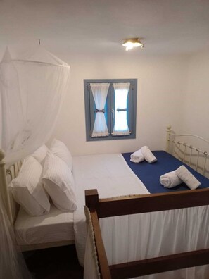 Ein Einzelbett mit Baldachin, ein kleines Fenster mit Vorhängen und ein Nachttisch mit Lampe.