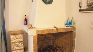 Una chimenea con revestimiento de ladrillo, un tapiz decorativo, un estante pequeño con una botella y un velero de juguete, y un aparador de madera con diseños.