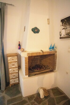 Ein Kamin mit Ziegelverkleidung, ein dekoratives Wandbild, eine kleine Ablage mit einer Flasche und einem Spielzeugsegelschiff sowie ein Holzkabinett mit Muster.