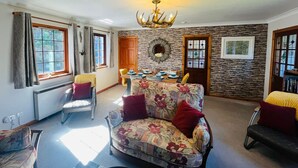 A living room with a sofa, chairs, a dining table, and a chandelier. - Braehead Cottage in Glencoe Village (Glencoe)