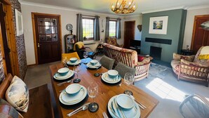 A dining area with a wooden table set for four, a sofa, and a fireplace. - Braehead Cottage in Glencoe Village (Glencoe)
