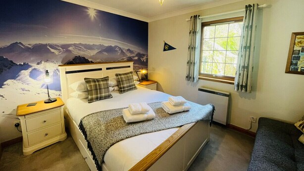 A bedroom with a bed, nightstands, a star-shaped ceiling light, a window with curtains, and a mountain mural on the wall. - Braehead Cottage in Glencoe Village (Glencoe)