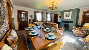 A dining area with a wooden table set for four, chairs, a chandelier, and a fireplace. - Braehead Cottage in Glencoe Village (Glencoe)