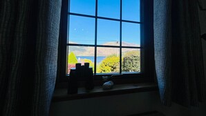 A window with a view of a landscape, curtains, and a small table with items on it. - Braehead Cottage in Glencoe Village (Glencoe)