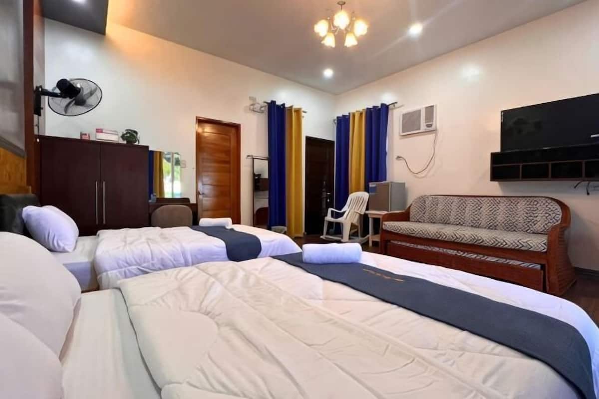 Una habitación de hotel con dos camas, un sofá, un escritorio, una silla, un televisor y cortinas.