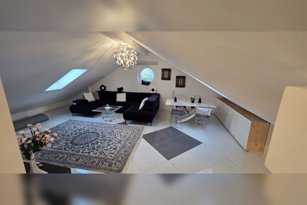 Ett sovrum på vinden med en svart soffa, ett matbord och en kristallkrona.