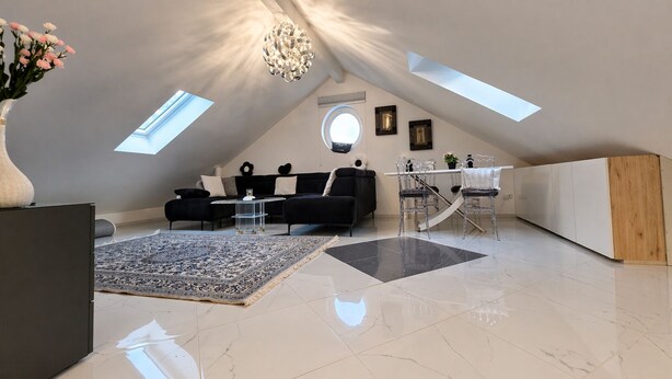 Un loft moderne avec de hauts plafonds, des fenêtres de toit, un coin repas et un salon agrémenté d’un grand tapis.