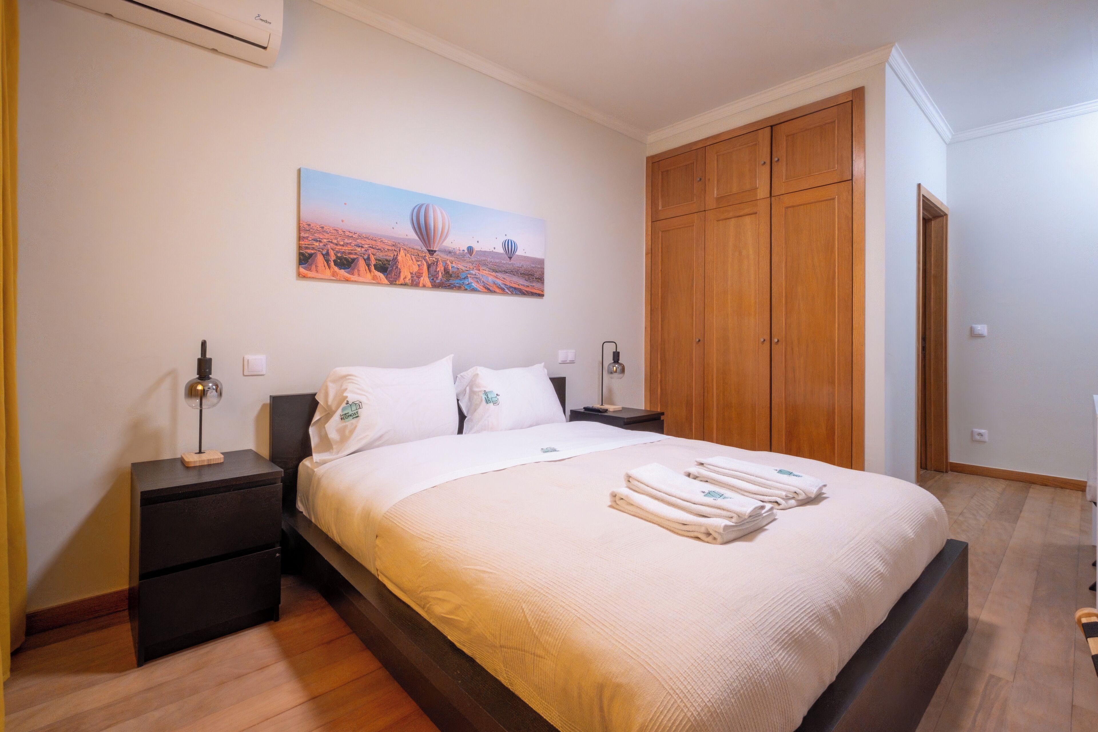 Un dormitorio con cama, mesitas de noche, un armario de madera y un cuadro en la pared.
