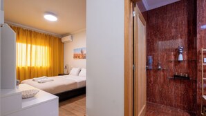A hotel room with a bed, a bedside table, a mirror, a bathroom with a shower, and a marble wall. - FamilyHub - EcoHost | T2+1 - 8 people - A/C - Porto (Senhora da Hora)