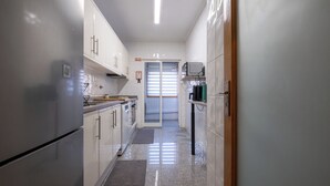 A narrow kitchen with white cabinets, a refrigerator, and a microwave. - FamilyHub - EcoHost | T2+1 - 8 people - A/C - Porto (Senhora da Hora)
