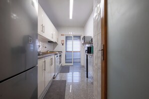 Eine schmale Küche mit weißen Schränken, einem Kühlschrank und einer Mikrowelle.