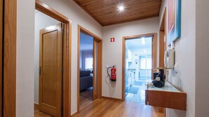 A hallway with wooden flooring, a fire extinguisher, a telephone, and a door leading to another room. - FamilyHub - EcoHost | T2+1 - 8 people - A/C - Porto (Senhora da Hora)