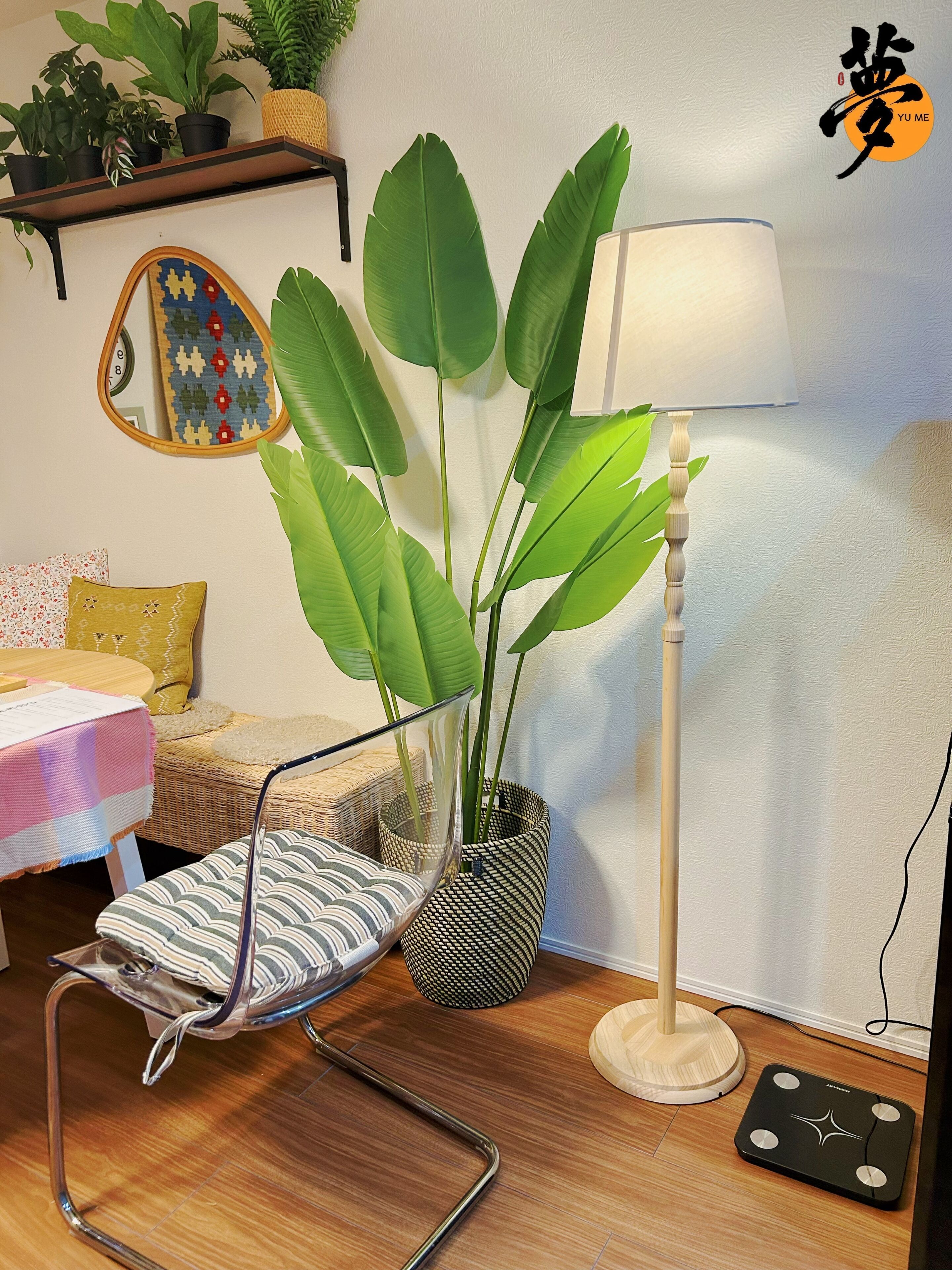A room with a chair, a floor lamp, a potted plant, a mirror, and a wall clock.