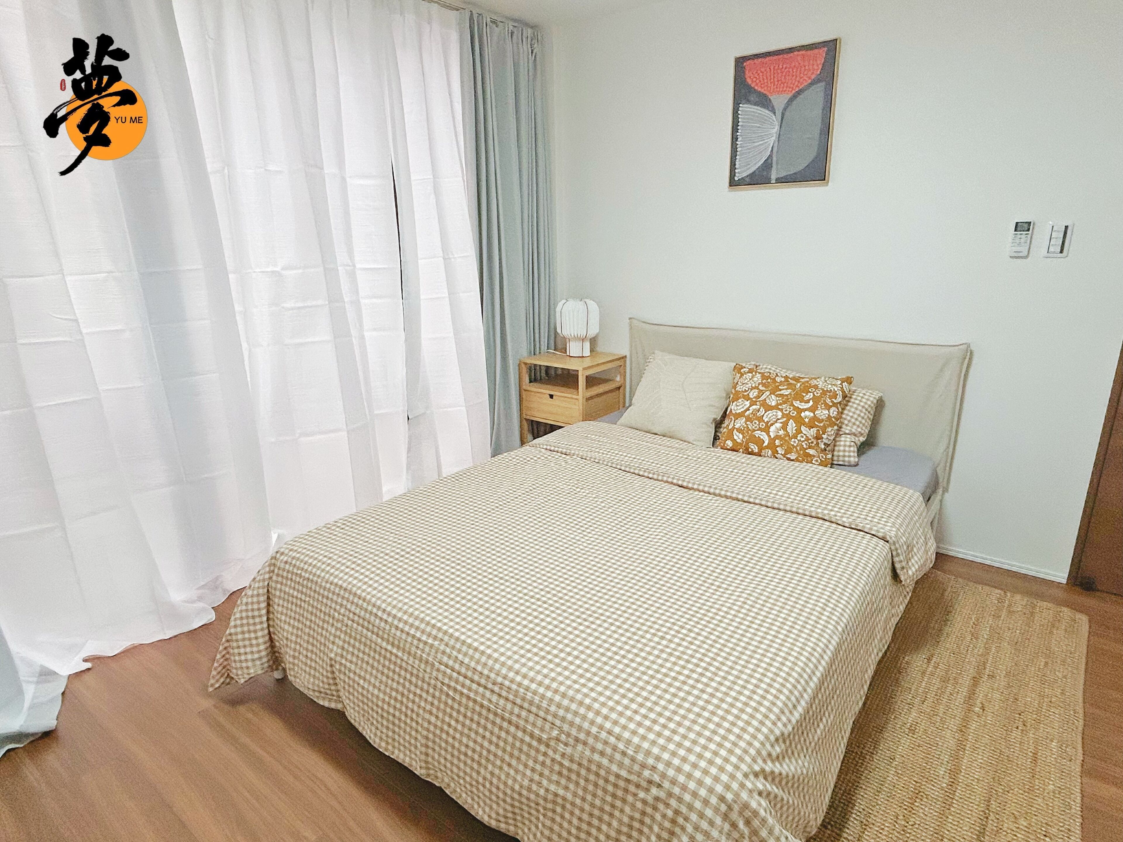 A bedroom with a bed, curtains, a bedside table, a nightstand, a pillow, a wall art piece, and a rug.