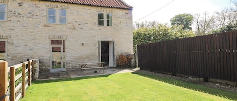 A stone building with a tiled roof, a wooden fence, and a grassy yard.