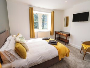 Un dormitorio con cama, escritorio, silla, ventana con cortinas y televisor.