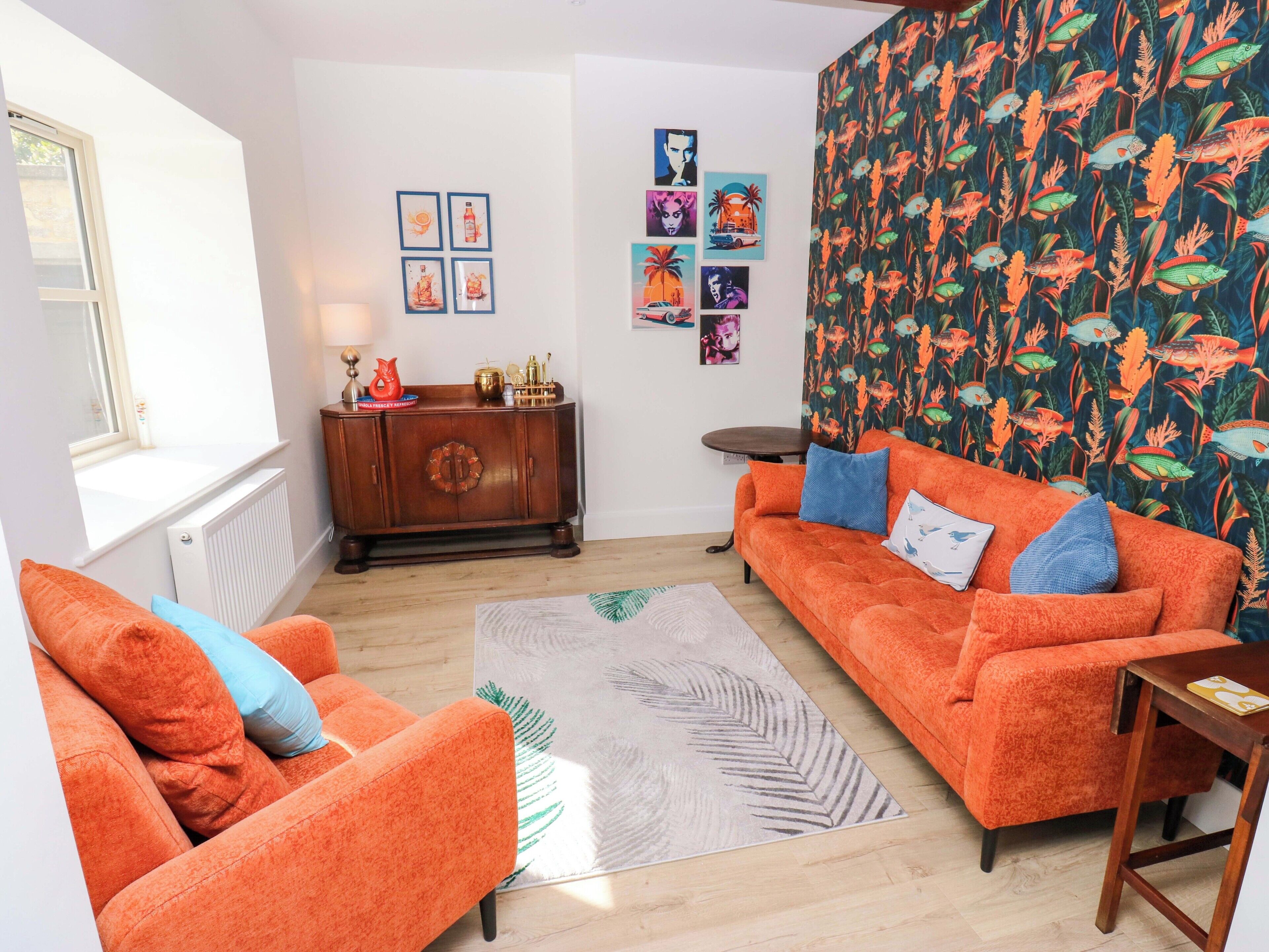 Een woonkamer met een bank, fauteuil en behang met een patroon.