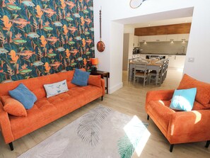 Ein Wohnzimmer mit zwei orangefarbenen Sofas, einer Wand mit Muster, einem Essbereich und einer Küche.