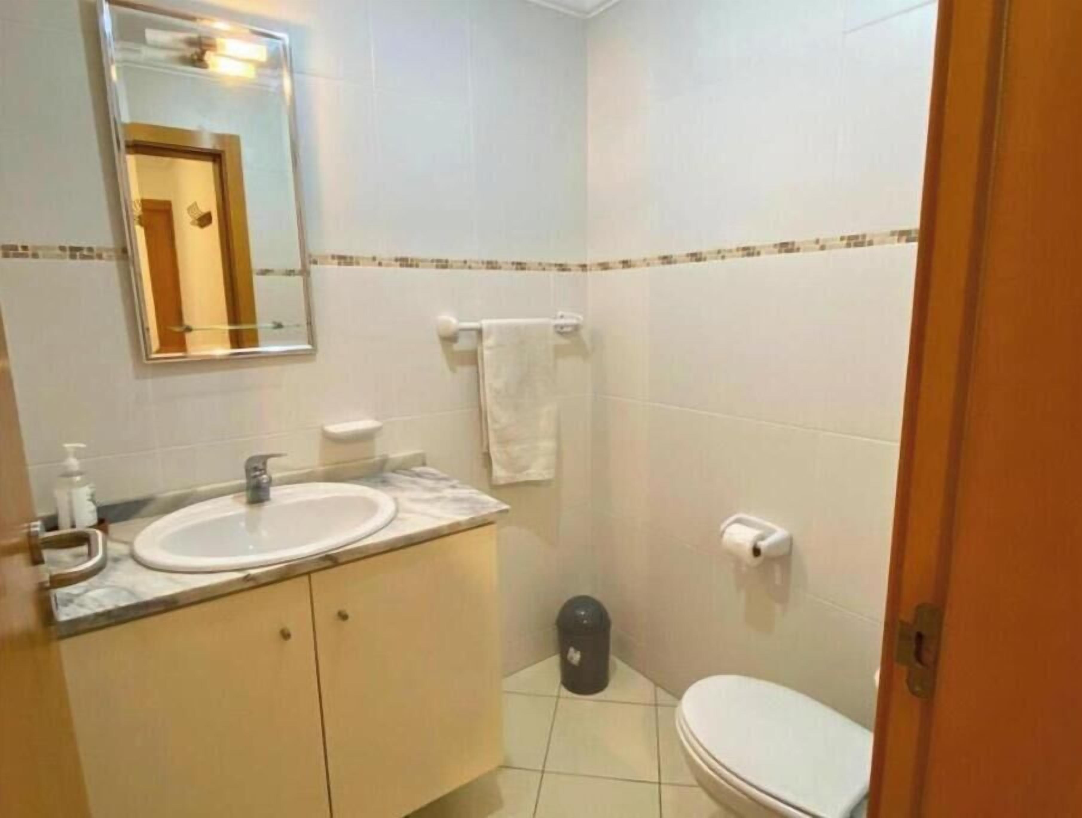 A bathroom with two sinks, a toilet, a trash bin, and a towel rack.