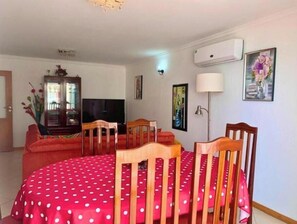 Ein Zimmer mit Esstisch, Stühlen, Fernseher, Schrank und Bildern an den Wänden.