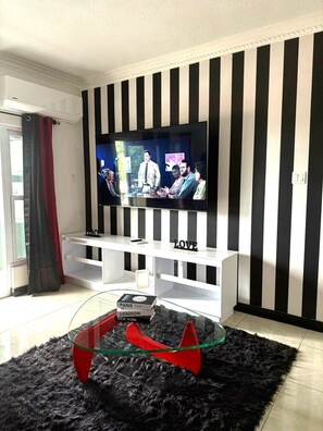 Ein Wohnzimmer mit einem Fernseher auf einem weißen Schrank, einem Glastisch mit roten Akzenten und einer schwarz-weißen Wand.