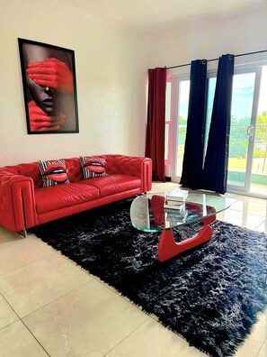 Ein rotes Sofa mit gestreiften Kissen, ein Glastisch, ein schwarzer Teppich und ein gerahmtes Bild an der Wand.