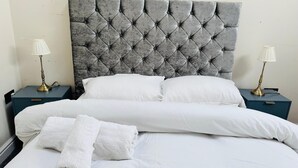 A neatly made bed with white linens, a tufted grey headboard, and two bedside tables with lamps.