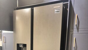 A stainless steel Samsung refrigerator with a freezer compartment, a water dispenser, and a handle on the top.