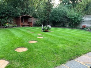 Une pelouse bien entretenue, agrémentée de pas japonais, d’une structure en bois et de diverses plantes.