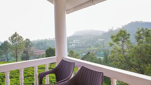 A balcony with wicker chairs, a white railing, and a view of a green landscape with hills. - Winterbourne Chalet 3-bedroom villa in pleasant Coonoor getaway (Coonoor)